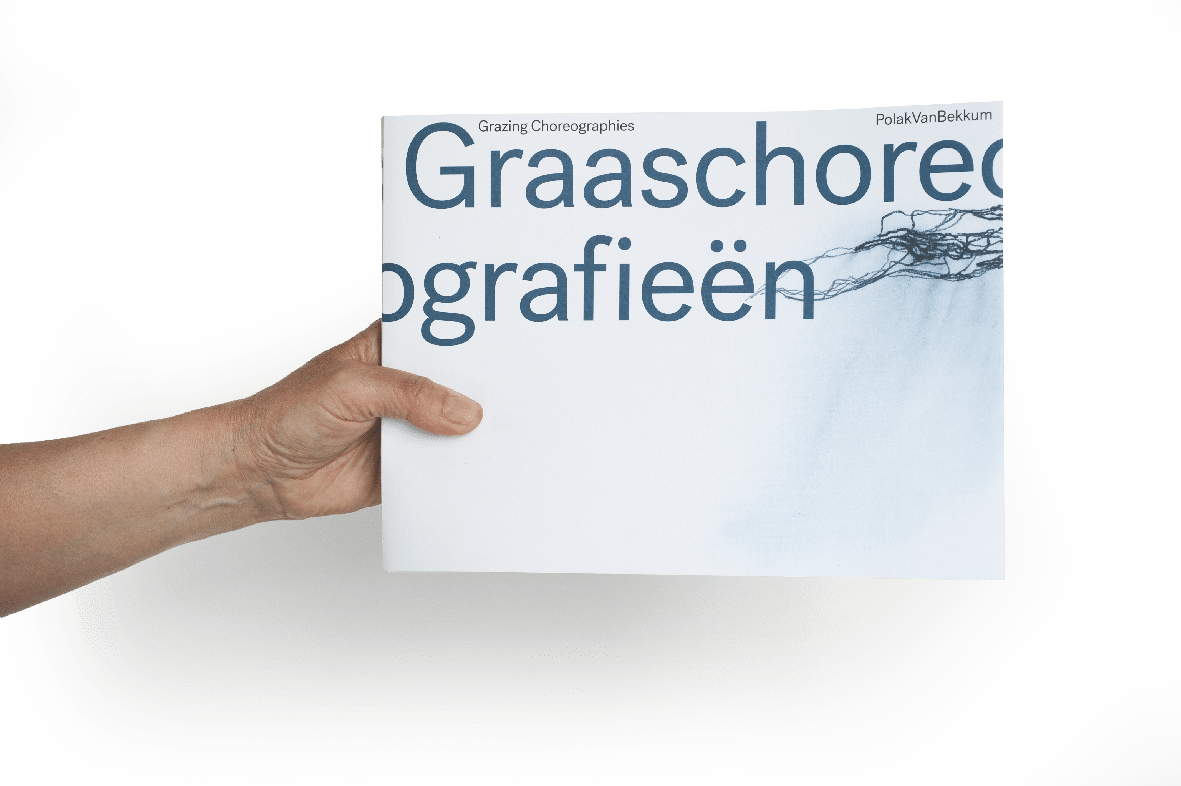 Een hand houdt het boek Graaschoreografieën op zodat de cover te zien is.
